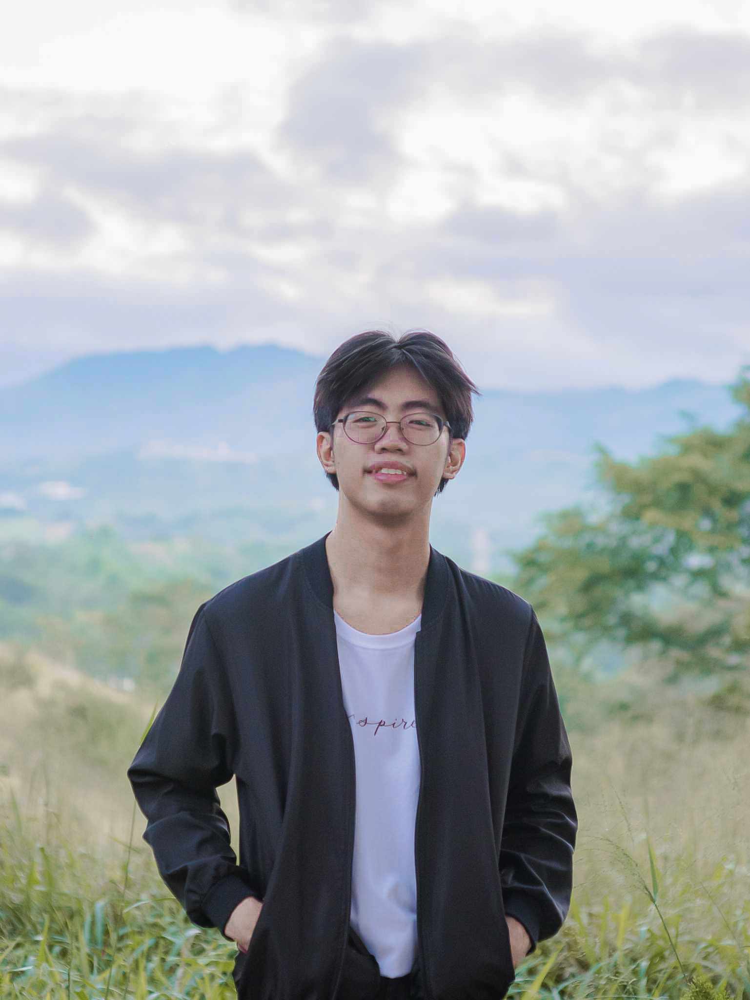 Jhestin Digap smiling in a black jacket, standing on a grassy hillside with mountains behind.