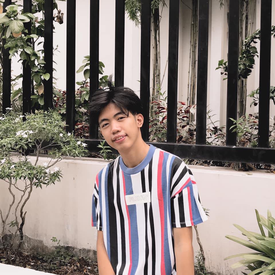 Jhestin smiling in a striped T-shirt in front of a garden fence.